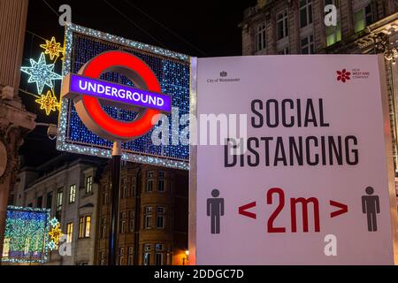 Londra, Regno Unito - 22 novembre 2020: Un segnale di allontanamento sociale, raffigurato accanto all'insegna della metropolitana di Londra alla stazione di Oxford Circus a Londra, Regno Unito. Foto Stock