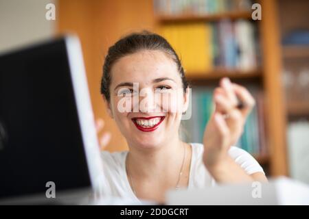 Giovane donna al computer in biblioteca, sorridente Foto Stock