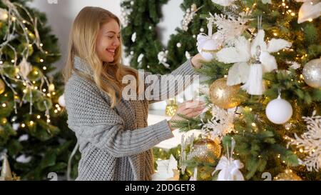 Felice giovane donna bionda che decora l'albero di natale con la sfera a. la sua casa Foto Stock