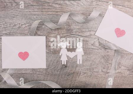 Una ragazza e un ragazzo da carta, una coppia amorevole su uno sfondo di legno e buste bianche per le lettere. San Valentino Foto Stock