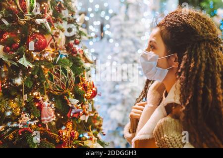 Bella donna afro capelli indossando maschera medica protettiva viso in negozio decorato a natale Foto Stock