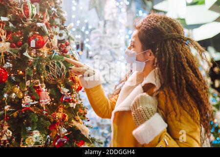 Bella donna afro capelli indossando maschera medica protettiva viso in negozio decorato a natale Foto Stock