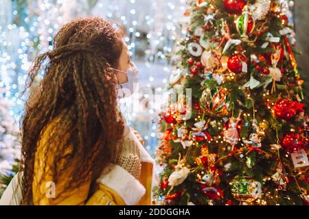 Bella donna afro capelli indossando maschera medica protettiva viso in negozio decorato a natale Foto Stock