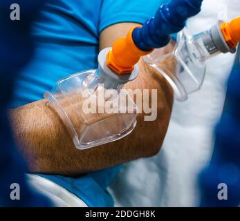 Paziente di sesso maschile non riconoscibile con ventose a vuoto sul braccio appoggiate panca durante la seduta di fisioterapia in ospedale Foto Stock