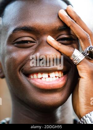 Bel maschio afroamericano con anelli alla moda sulle dita che toccano faccia e sorride alla macchina fotografica Foto Stock