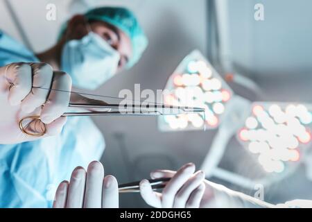 Dal basso, vista laterale del chirurgo professionale con medico forbici che lavorano in sala operatoria in un moderno ospedale Foto Stock