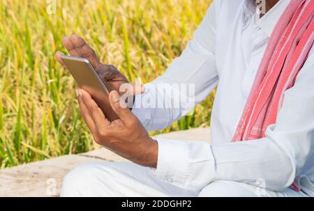 Primo piano di mani di carestia indiana utilizzando mobile vicino agricolo Fattoria terra - anziani hsnds villager utilizzando il telefono - concetto di gente rurale anziana usando Foto Stock