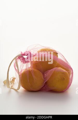 Ancora vita con i limoni in borsa di tessuto a rete rosa retroilluminata su sfondo bianco Foto Stock