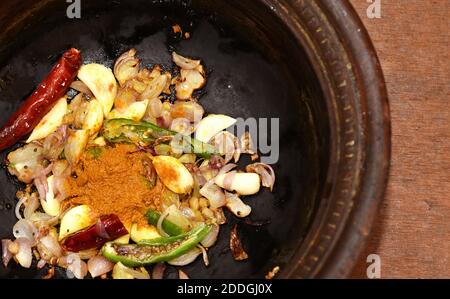 Saltando o saltando in una padella di fango aglio, curcuma, cipolle, peperoncino verde e senape in olio in un piatto di fango.cucina indiana del sud ricette. Foto Stock