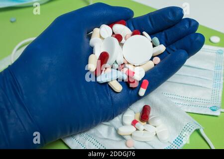 Vista dall'alto di una mano guanto riempita di farmaco su un tavolo verde con una maschera chirurgica. Uso responsabile dei medicinali. Foto Stock