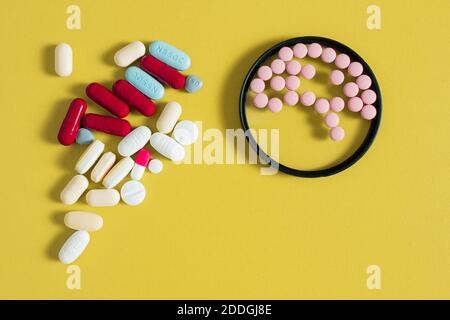 Le piccole pillole rotonde simulano la forma del cervello all'interno di un cerchio e un mazzo di farmaci diversi su una tabella di colore senape. Concetto di assistenza sanitaria. Foto Stock