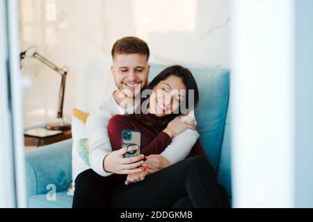 Coppia amorevole positiva che riposa sul divano e prende selfie sopra smartphone e divertimento insieme Foto Stock