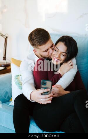 Coppia amorevole positiva che riposa sul divano e prende selfie sopra smartphone e divertimento insieme Foto Stock