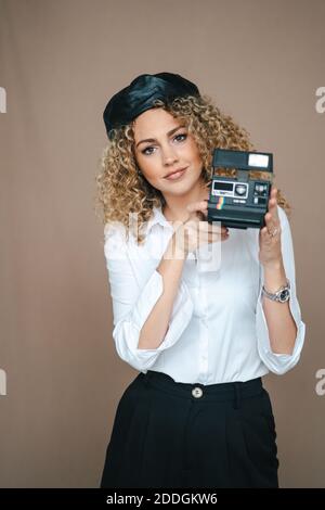 Fotografo femminile con fotocamera retrò istantanea per scattare foto sfondo marrone in studio Foto Stock