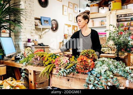 Fiorista professionista che organizza bouquet di fiori mentre lavora in negozio su tavolo di legno Foto Stock