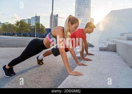 Vista laterale completa del corpo di determinati giovani attivi e donne in abbigliamento sportivo che spingono contro i passi concreti durante l'allenamento fitness insieme su ci Foto Stock