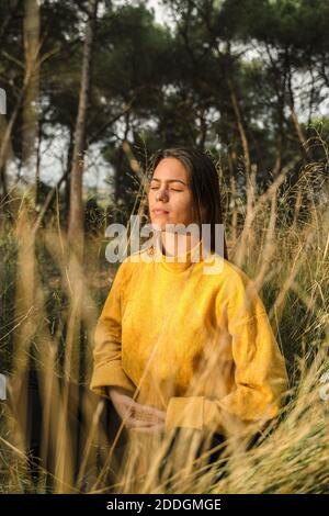 Tranquilla donna seduta in campo asciutto e godendo il tramonto dentro campagna con occhi chiusi mentre meditating Foto Stock