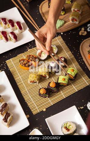 Dall'alto del prodotto mano irriconoscibile con i chopsticks che prendono assortiti sushi vegetariano da stuoia di bambù Foto Stock