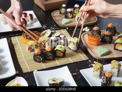 Da sopra di raccolto gente irriconoscibile con i chopsticks che prendono assortiti sushi vegetariano da stuoia di bambù Foto Stock