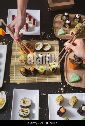 Da sopra di raccolto gente irriconoscibile con i chopsticks che prendono assortiti sushi vegetariano da stuoia di bambù Foto Stock