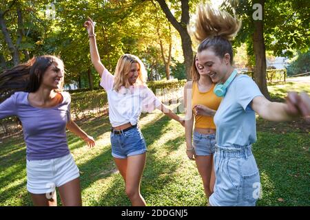 Gruppo di ridere multiracial teen femmina amici che hanno divertimento e. ballare insieme mentre si passa la giornata estiva nel parco verde Foto Stock