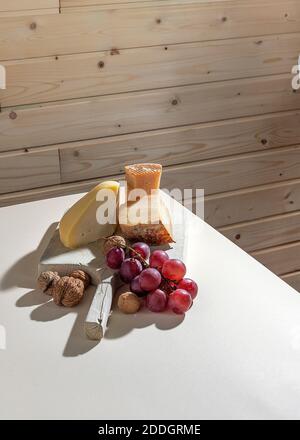 Composizione rustica con formaggio artigianale aromatico servito con rosso maturo uva e noci su tavola bianca vicino a parete di legno Foto Stock