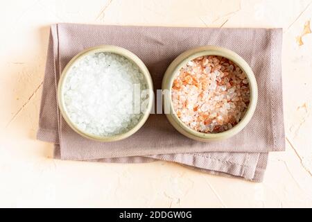 Sale rosa di roccia dell'Himalaya e sale minerale bianco in ciotole di ceramica e cucchiaio su sfondo chiaro. Vista dall'alto. Foto Stock