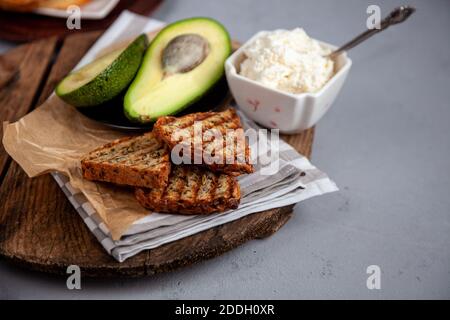 Panini con formaggio morbido, avocado e cetriolo. La colazione è sul tavolo. Cibo sano. Tostare e spalmare su di esso. Avocado sandwich vita morta Foto Stock