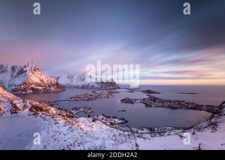 Fantastica alba viola vista dalla vetta di Reinebringen. Vista sul lago Reinive, il villaggio di Reine e il fiordo durante l'inverno innevato. Lofoten, Norvegia Foto Stock