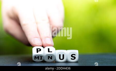 La mano trasforma i dadi e cambia la parola meno in più. Foto Stock