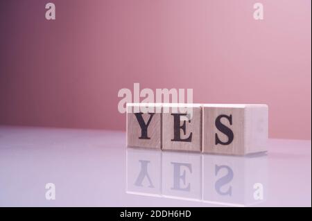 Testo sì su blocchi di cubi di legno. Le lettere sì scritte sui cubi in lettere nere isolate su una superficie di vetro. SÌ testo per il tuo desing. Foto Stock