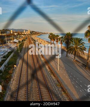 Ferrovia e spiaggia di Badalona attraverso lo sbiadimento del metallo recinzione Foto Stock
