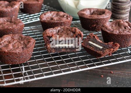 Oreo Stuffed Brownie Cups: Coppe di brownie riempite con una griglia di raffreddamento del filo del biscotto sandwich con una ciotola di glassa sullo sfondo Foto Stock