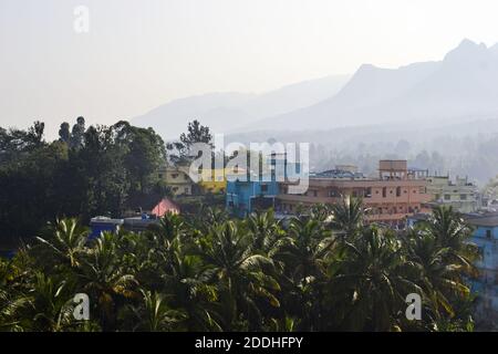 Palme e case colorate contro la vista panoramica mattina della catena montuosa in foschia. Paesaggio tropicale, Sultano Bathery, Kerala, India. Foto Stock