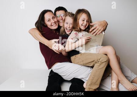 Felice famiglia seduta insieme sul tavolo. Papà abbraccava moglie e bambini nel suo abbraccio Foto Stock