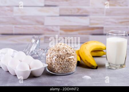 Frittelle OAT con banana. Processo di cottura passo dopo passo. Ingredienti vista dall'alto. Banane, latte, uova, avena, sale. Tavolo di legno sfondo. Spazio di copia Foto Stock