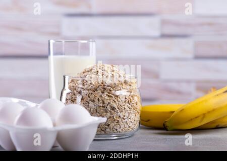 Frittelle OAT con banana. Processo di cottura passo dopo passo. Ingredienti vista dall'alto. Banane, latte, uova, avena, sale. Tavolo di legno sfondo. Spazio di copia Foto Stock