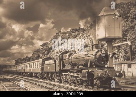 Vista laterale di Seppia di un treno a vapore d'epoca britannico che passa accanto alla torre dell'acqua a Bewdley, una delle stazioni di treni a vapore della Severn Valley. Foto Stock