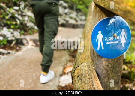 Cartello rotondo blu su recinto di legno vicino ad un parco sentiero che informa le persone di mantenere 2 metri 6 piedi fisico distanza sociale l'uno dall'altro, prevenire e proteggere Foto Stock