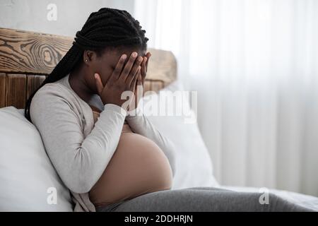 Cambiamenti emotivi durante la gravidanza. Donna incinta nera sconvolto coprendo il viso con le mani Foto Stock