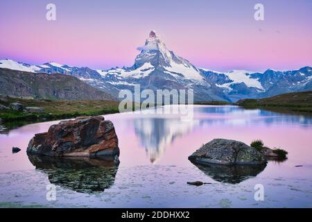 La cima del monte Cervino all'alba con riflesso nelle acque del lago di Stellisee con grandi rocce in primo piano a Zermatt in Svizzera. Foto Stock