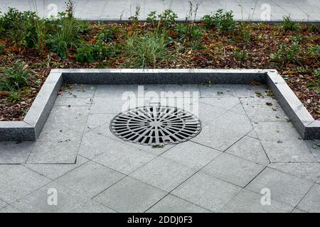 copertura tombino tondeggiante in metallo nero miglioramento del territorio città marciapiede pedonale del parco pavimentato con piastrelle grigio granito con pietra primo piano del bordo Foto Stock