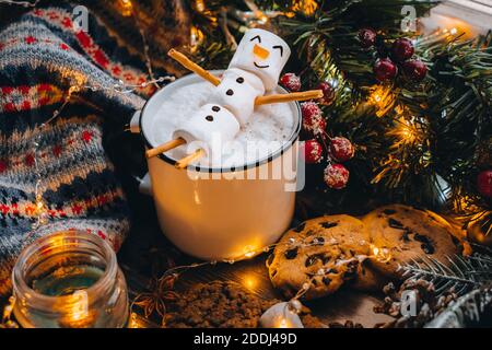 Tazza bianca di cibo di Natale con marshmallows di pupazzo di neve al cioccolato caldo. Biscotti fatti in casa, bastoni di cannella rami di abete xmas con luci calde di ghirlanda. Est Foto Stock