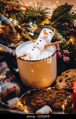 Tazzina bianca di cibo di festa con marshmallows caldi del pupazzo di neve di cacao del cioccolato. Biscotti dolci fatti in casa, bastone di cannella abete xmas tree luci calde del garland. Felice N Foto Stock