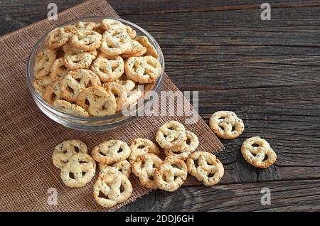 Pretzel salati con formaggio e semi in recipiente di vetro su tavolo di legno. Gustoso spuntino per la birra Foto Stock