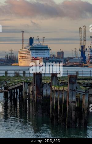 Una nave da crociera accanto al porto di Southampton ormeggia al tramonto con un vecchio molo e pile di legno in primo piano Foto Stock