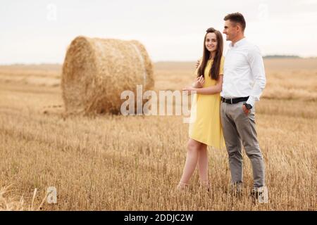 Foto di gioiosa coppia uomo e donna che camminano attraverso il campo d'oro con un mazzo di fiati e si abbracciano insieme durante il giorno di sole. Foto Stock