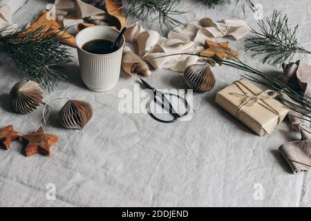 Natale festa composizione della natura morta. Tazza di caffè, carta ornamenti natalizi e confezione regalo. Nastri di velluto, rami di pino con forbici Foto Stock