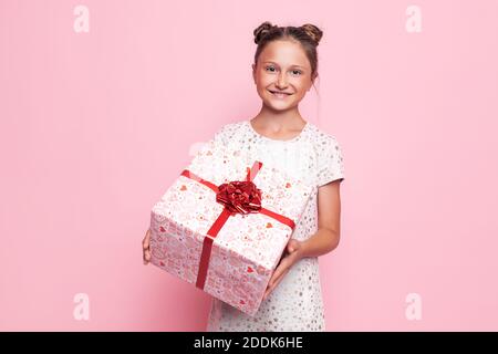 Ritratto di una ragazza adolescente felice con una confezione regalo nelle sue mani su uno sfondo rosa Foto Stock