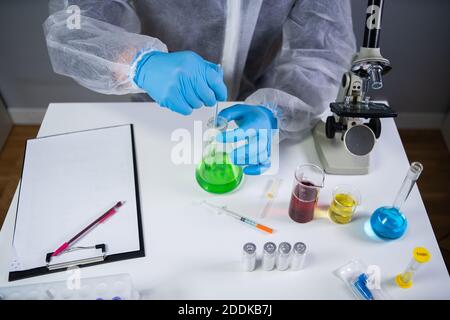 Tecnico di abbigliamento protettivo agitare a mano e agitare liquido verde in matraccio di Erlenmeyer in laboratorio chimico. Studi di tecnici di laboratorio Foto Stock